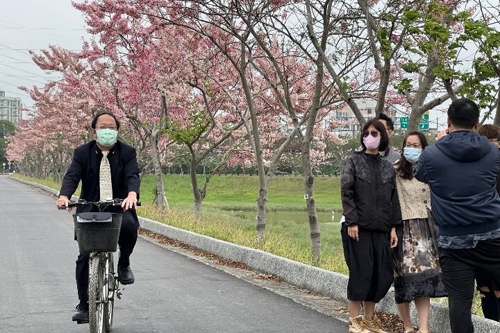 中華醫大校長孫逸民(左)單車遊逛仁德滯洪池畔與賞花民眾分享花旗木花開盛景